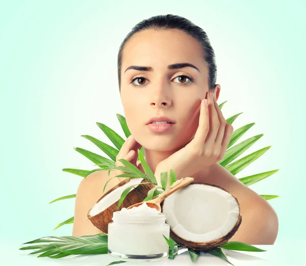 Kokosöl für die Haut. junge Frau und Kosmetik auf farbigem Hintergrund — Stockfoto