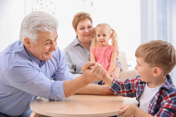 Lycklig äldre man och hans sonson med armbrytning tävling hemma — Stockfoto