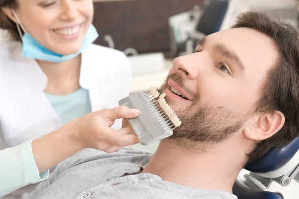 Dentist checking and selecting color of young man's teeth, closeup — Stock Photo, Image