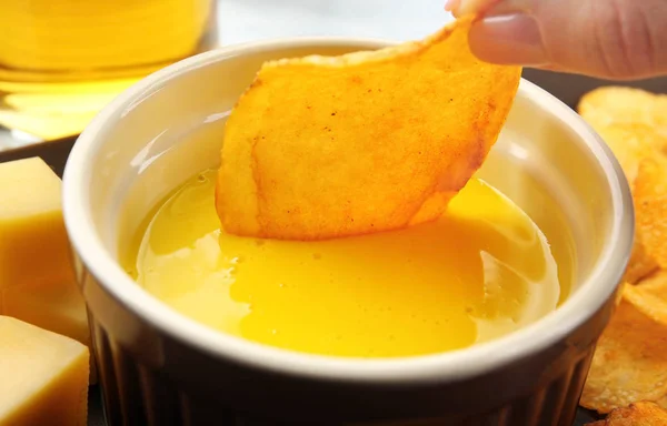 Woman dipping chips into bowl with creamy cheese sauce, close up — Stock Photo, Image