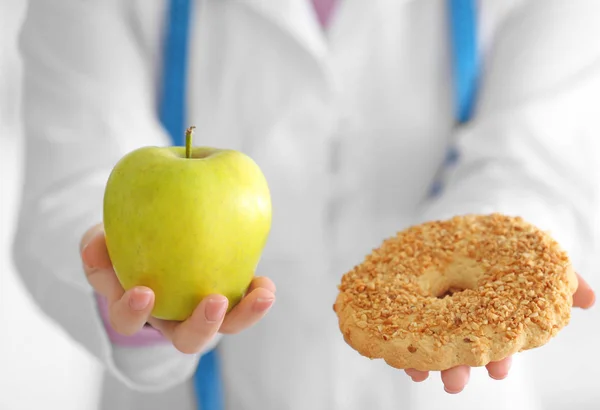 Unga kvinnliga nutritionist holding apple och cookie — Stockfoto