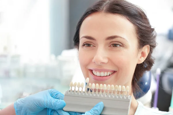 Dentist checking and selecting color of young woman's teeth — Stock Photo, Image