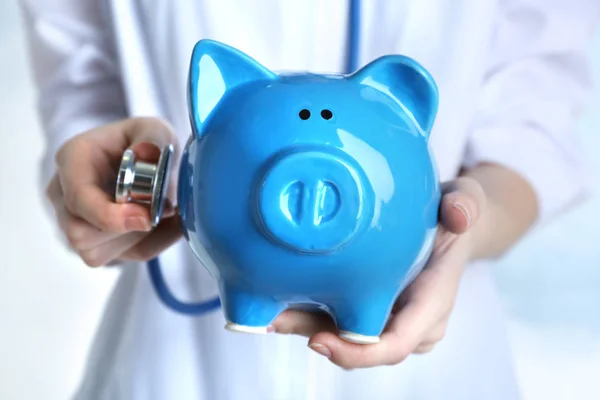 Female doctor holding piggy bank and stethoscope, close up. Concept of medical insurance — Stock Photo, Image