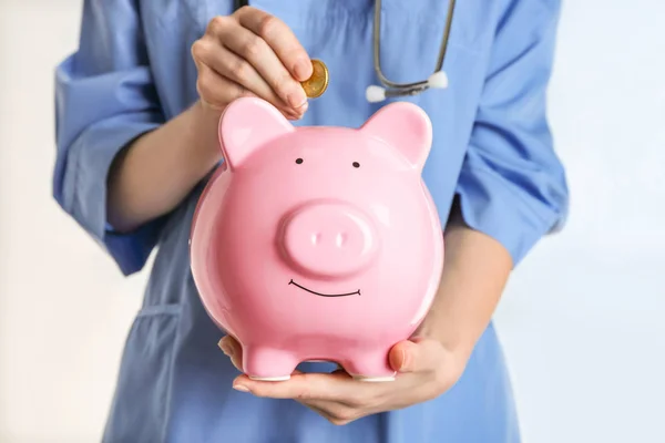 Doctora poniendo moneda en alcancía, de cerca. Concepto de seguro médico —  Fotos de Stock