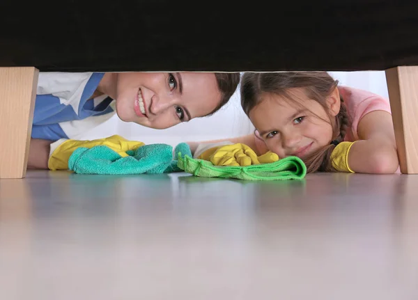 Kleine dochter en moeder reiniging van de vloer onder meubels — Stockfoto