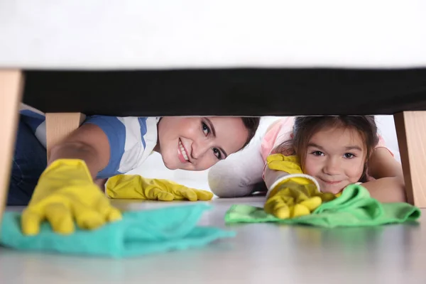 Kleine Tochter und Mutter putzen Fußboden unter Möbeln — Stockfoto