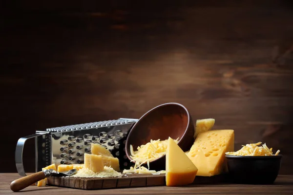 Composição de ralador, tábua de corte e tigelas com queijo sobre fundo de madeira — Fotografia de Stock