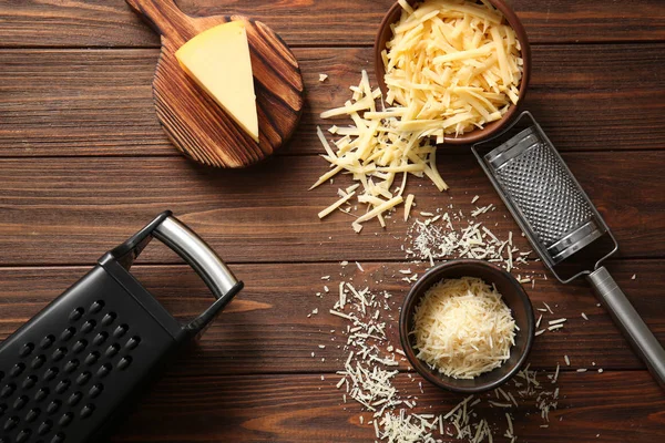 Grateadores, tigelas com queijo e tábua de corte sobre fundo de madeira — Fotografia de Stock