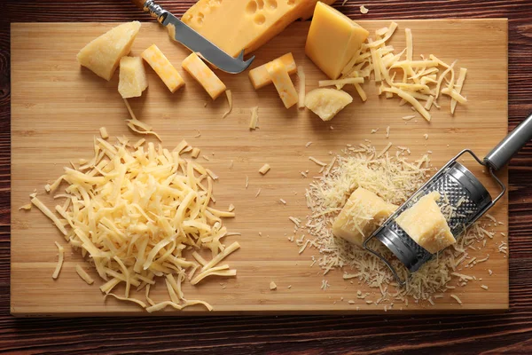 Planche à découper avec fromage, râpe et couteau sur fond bois — Photo