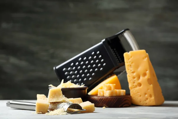 Grater and pieces of cheese on grey background — Stock Photo, Image