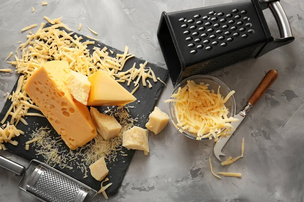 Prato de ardósia, tigela com queijo, grades e faca sobre fundo cinza — Fotografia de Stock