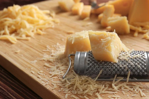 Tábua de corte com queijo e ralador em fundo de madeira — Fotografia de Stock