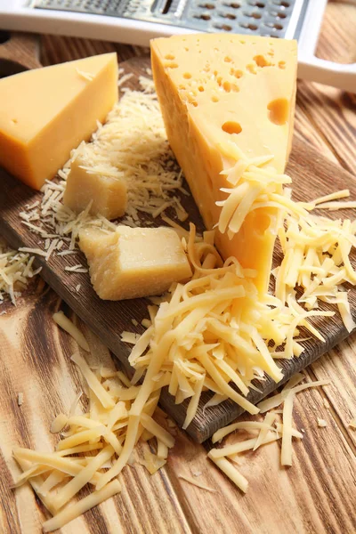 Tábua de corte com queijo e ralador em fundo de madeira — Fotografia de Stock