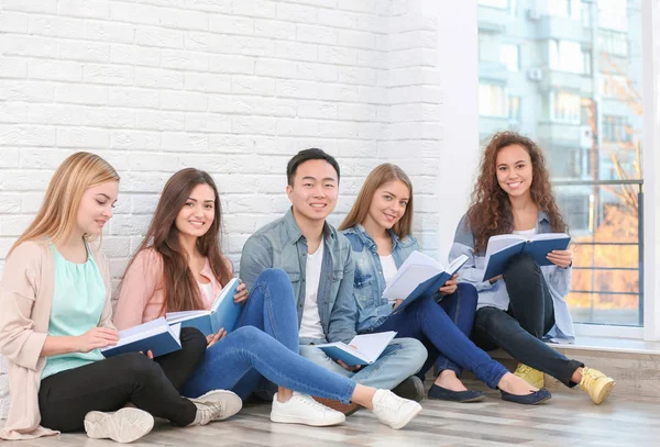 Groep mensen die het lezen van boeken zittend op de vloer in de buurt van bakstenen muur — Stockfoto