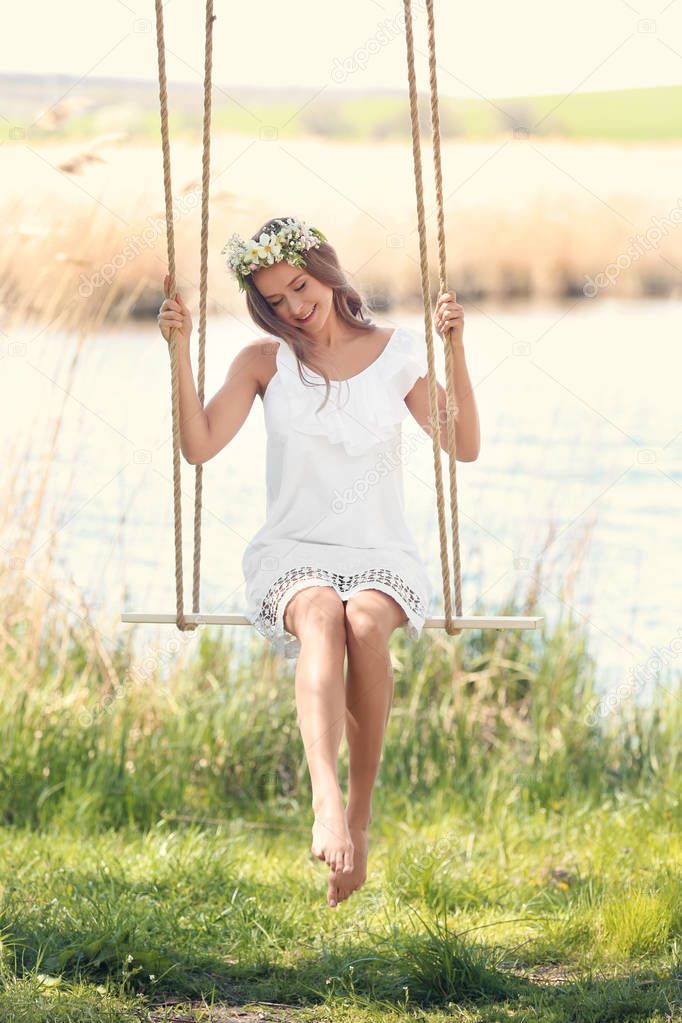 Beautiful young woman on swing near river