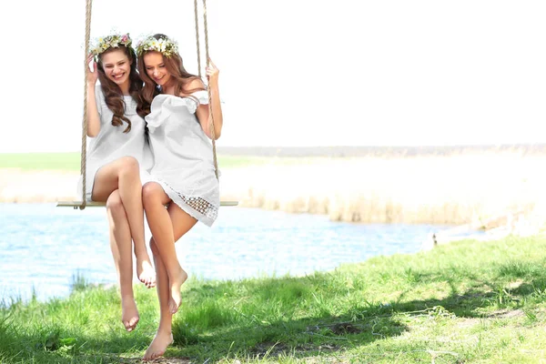 Dvě krásné mladé ženy na houpačce poblíž řeky — Stock fotografie
