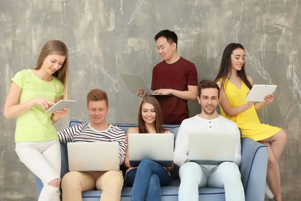 Mladí lidé s miniaplikacemi sedí na pohovce — Stock fotografie