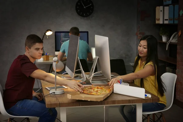 Young programmers eating pizza while working in office