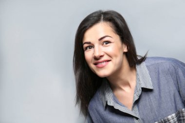 Gri arka plan üzerinde mutlu gülümseyen genç kadın portresi