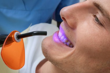 Dişçi klinikte hasta dişlerini muayene ediyor.