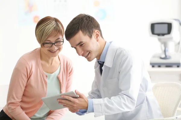 Jonge oogarts met tablet pc en volwassen patiënt in kliniek — Stockfoto