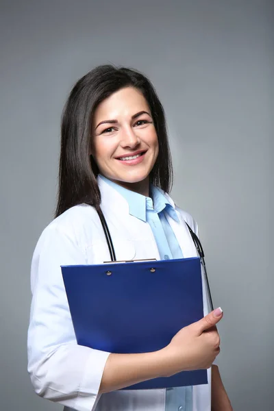 Mooie jonge dokter houd van Klembord op grijze achtergrond — Stockfoto