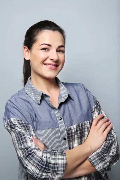 Portrait de belle jeune femme souriante avec les mains croisées sur fond gris — Photo