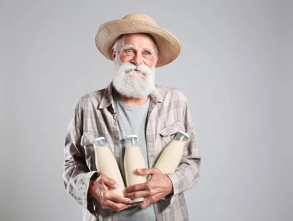 Hombre mayor con botellas de leche sobre fondo gris —  Fotos de Stock