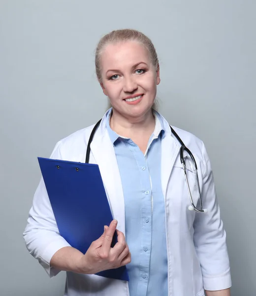 Portrait of smiling female doctor holding clipboard on grey background — Stock Photo, Image