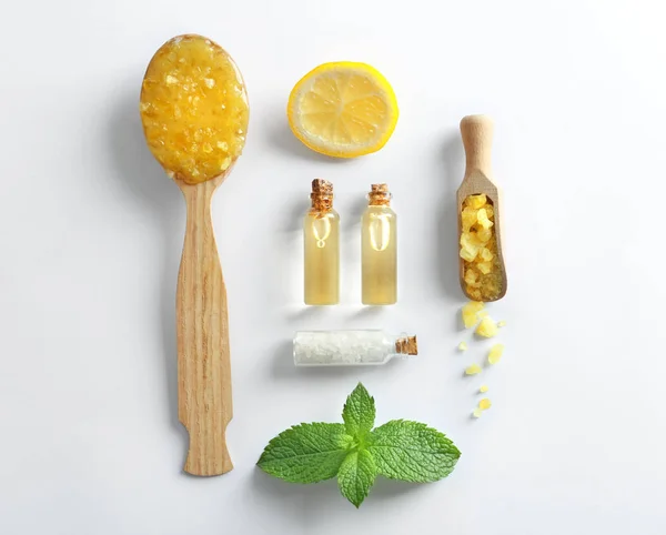 Cuchara de madera con exfoliante, rodaja de limón, menta, sal marina y botellas de aceite aisladas en blanco — Foto de Stock