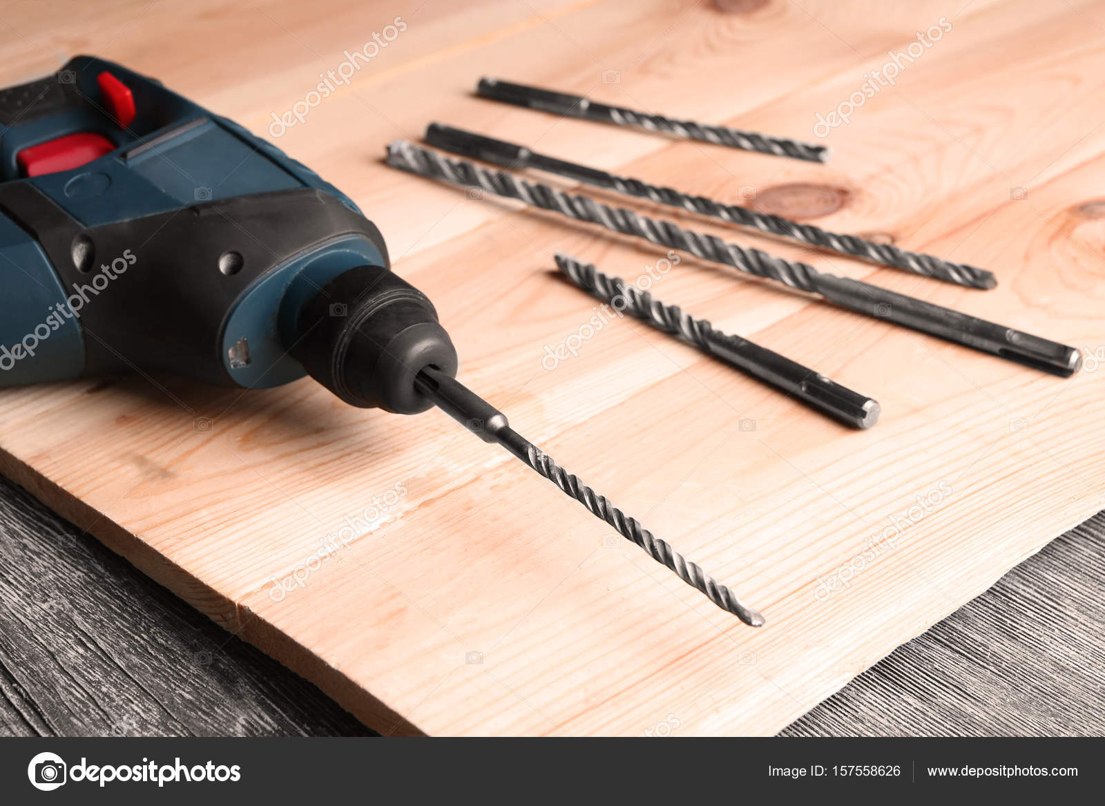 Drill, attachments and wooden board on table in carpenter's