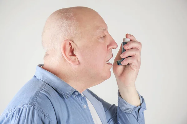 Hombre mayor usando inhalador de asma sobre fondo claro —  Fotos de Stock