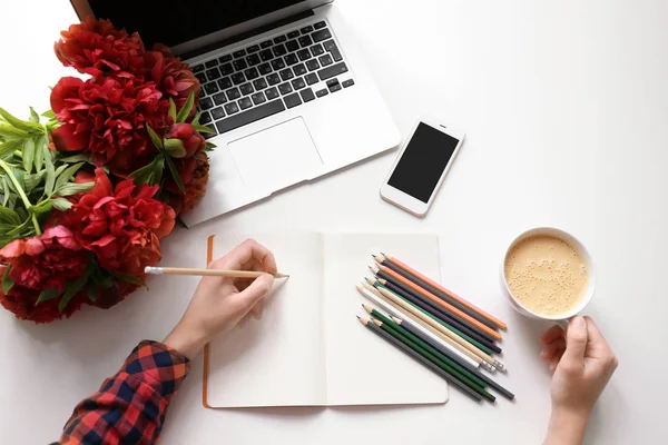 Vrouw in notitieblok openen puttend uit tabel met mooie pioenrozen — Stockfoto