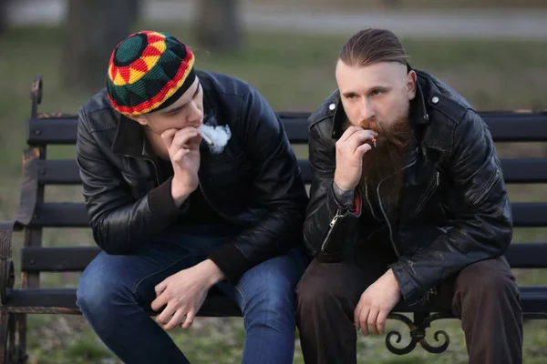 दो पुरुष बाहर बेंच पर बैठे हुए घास धूम्रपान करते हुए — स्टॉक फ़ोटो, इमेज