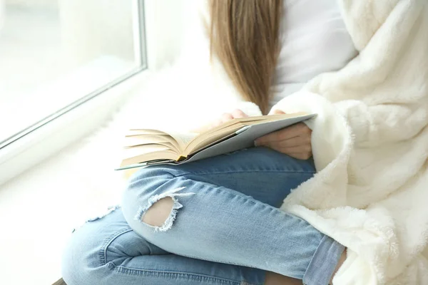 Belle jeune femme lisant le livre près de la fenêtre à la maison, gros plan — Photo