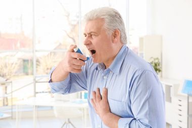 Elderly man using inhaler in clinic clipart