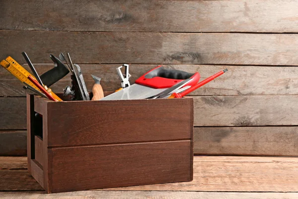 Vak met carpenter's tools op tafel tegen houten achtergrond — Stockfoto