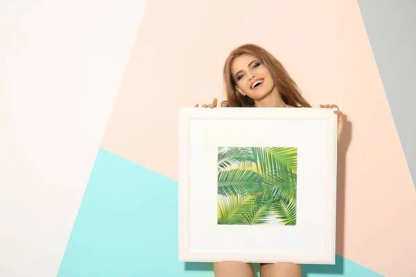 Vacker ung kvinna håller bilden med tropic växter stående nära färg vägg — Stockfoto