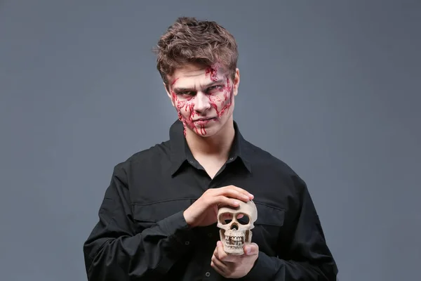 Young man with Halloween makeup and skull on grey background — Stock Photo, Image