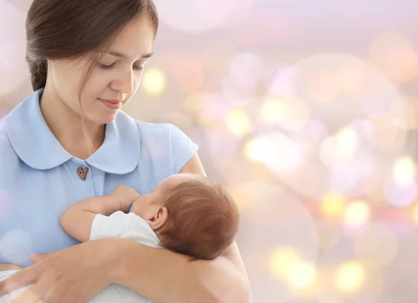 Wanita muda menggendong bayi yang sedang tidur dengan latar belakang lampu yang kabur. Konsep perayaan hari libur — Stok Foto