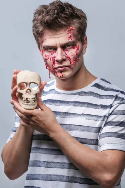 Young man with Halloween makeup and skull on light background