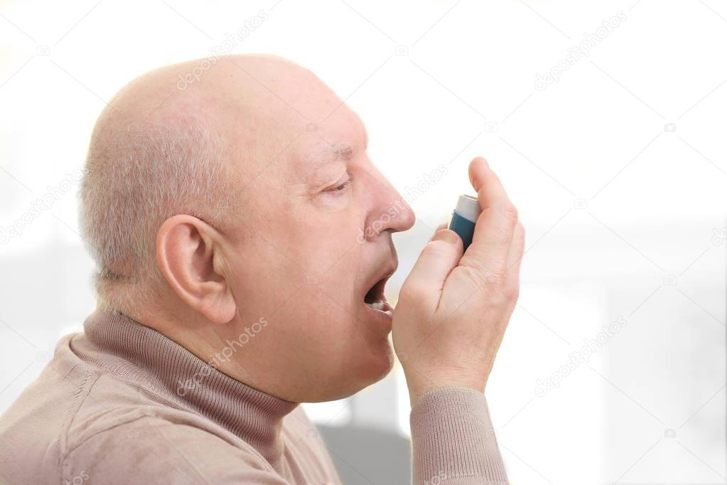 Senior man using asthma inhaler on light background