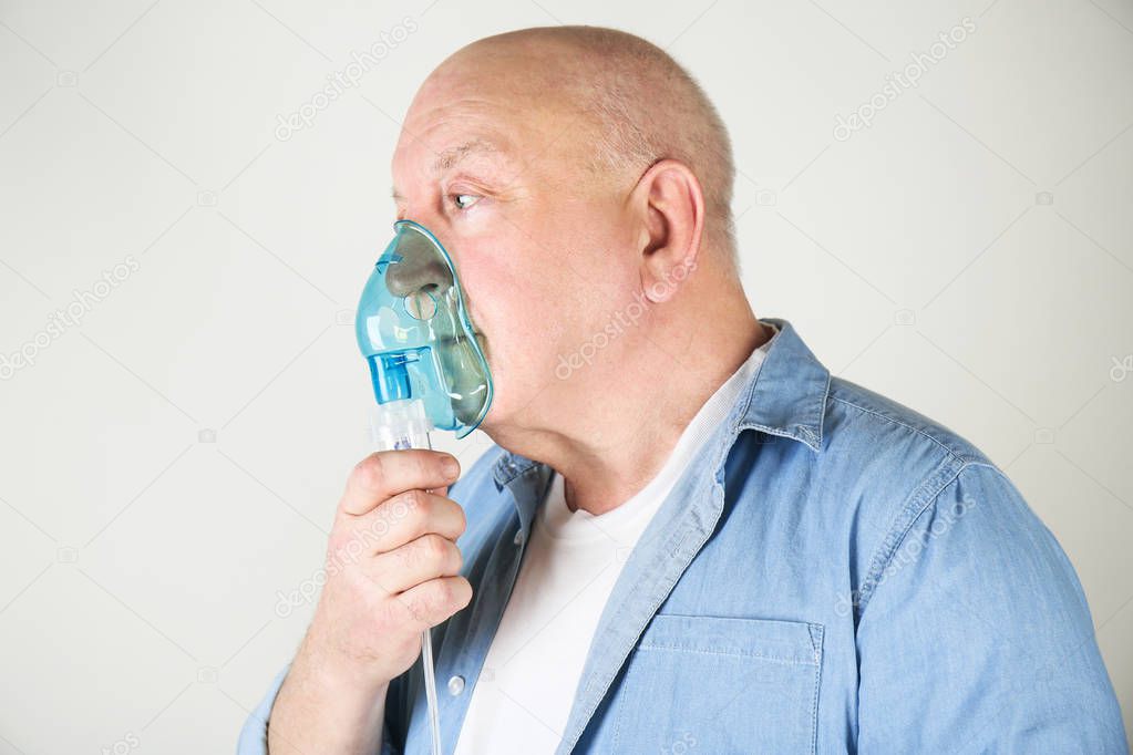 Senior man using asthma machine on light background