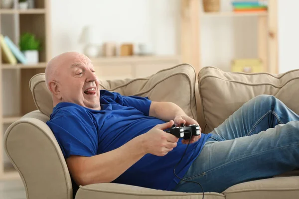 Gordo hombre mayor jugando videojuego mientras está acostado en el sofá en casa. Concepto sedentario estilo de vida — Foto de Stock