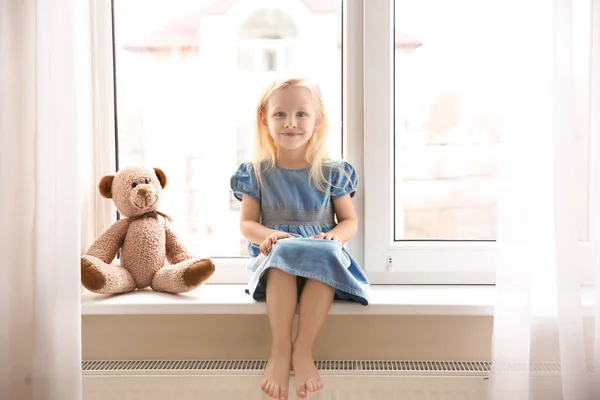 Petite fille mignonne assise sur le rebord de la fenêtre — Photo