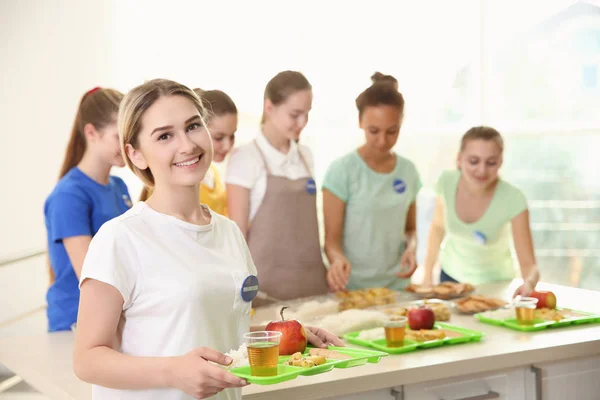 Joven voluntaria y su equipo cerca de la mesa con diferentes productos en el interior —  Fotos de Stock