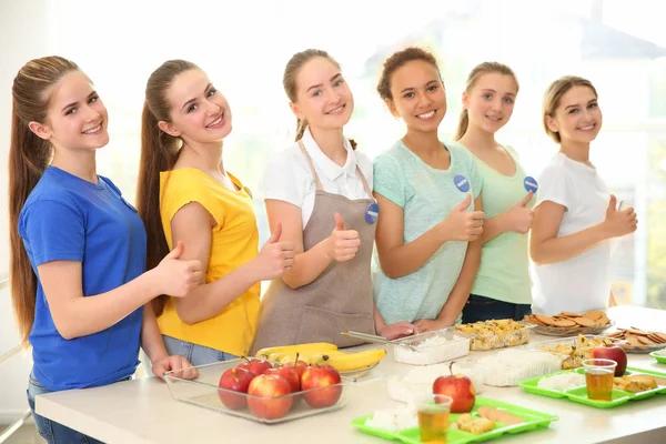 Young volunteers near table with different products indoors — Stock Photo, Image