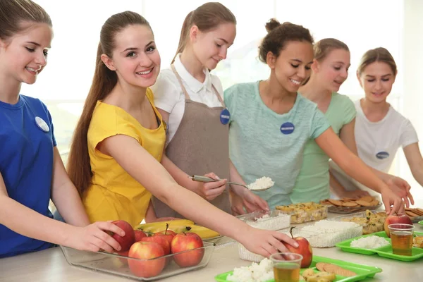 Young volunteers near table with different products indoors — Stock Photo, Image