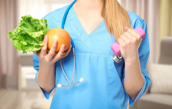 Conceito de perda de peso. Jovem nutricionista com alimentos e halteres no fundo embaçado — Fotografia de Stock