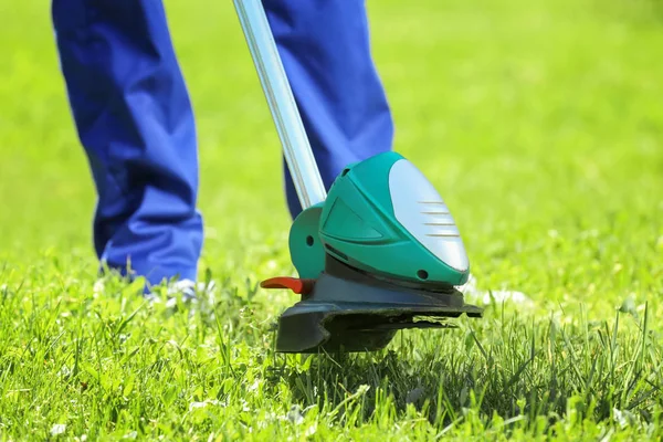 worker mowing lawn with grass trimmer